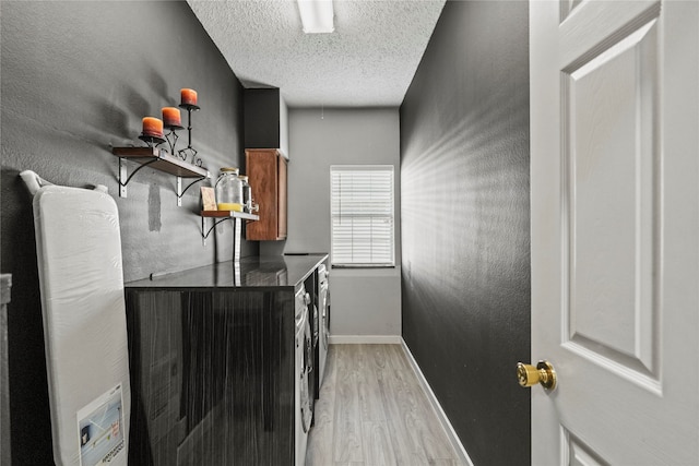 washroom featuring water heater, light hardwood / wood-style floors, washer and clothes dryer, and a textured ceiling