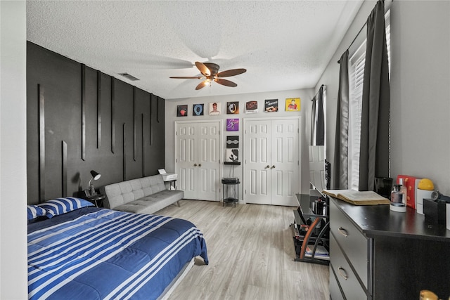 bedroom with a textured ceiling, light hardwood / wood-style floors, ceiling fan, and multiple closets