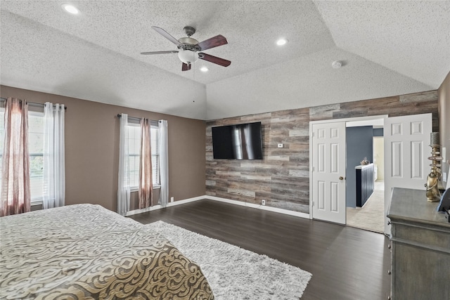 bedroom with a textured ceiling, lofted ceiling, ceiling fan, wooden walls, and dark hardwood / wood-style floors