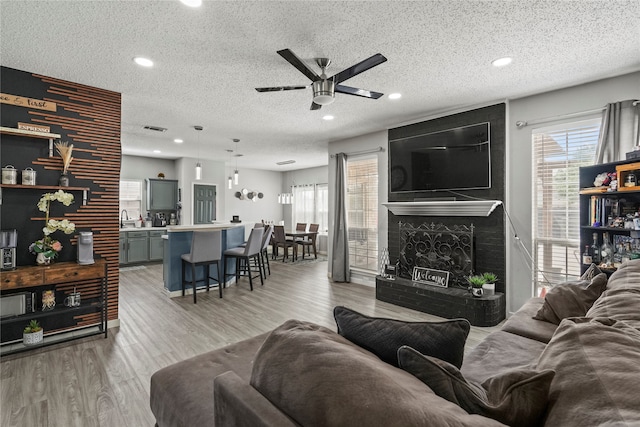 living room featuring light wood-type flooring, a textured ceiling, a fireplace, and ceiling fan