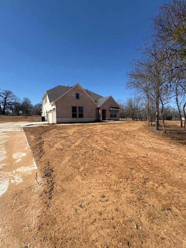 view of side of property featuring a garage, brick siding, and a shingled roof