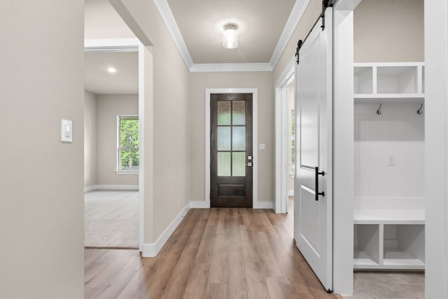 interior space featuring crown molding, light wood-type flooring, a barn door, and baseboards