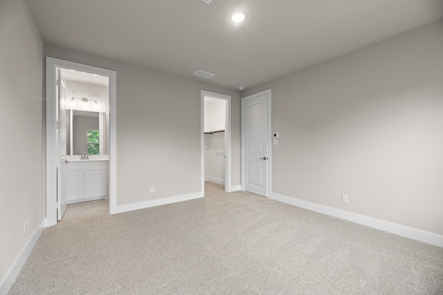 unfurnished bedroom with baseboards, a spacious closet, light carpet, and visible vents