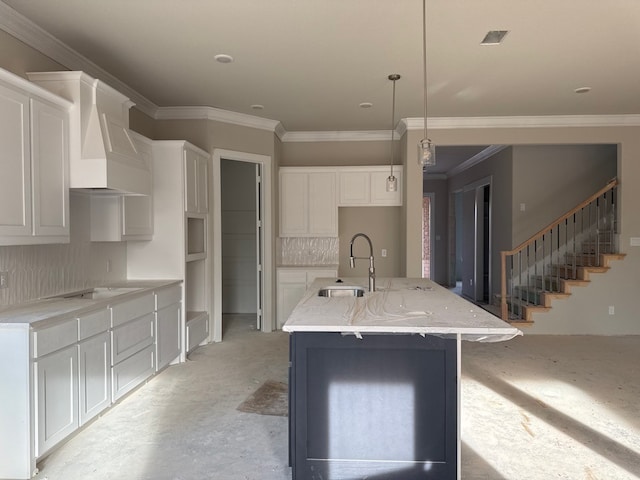 kitchen featuring custom exhaust hood, a kitchen island with sink, sink, hanging light fixtures, and white cabinetry