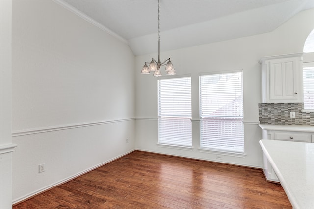 unfurnished dining area with a notable chandelier, ornamental molding, lofted ceiling, and dark hardwood / wood-style floors