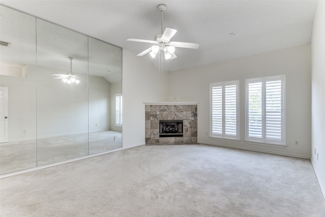 unfurnished living room with ceiling fan, vaulted ceiling, a tile fireplace, and light colored carpet