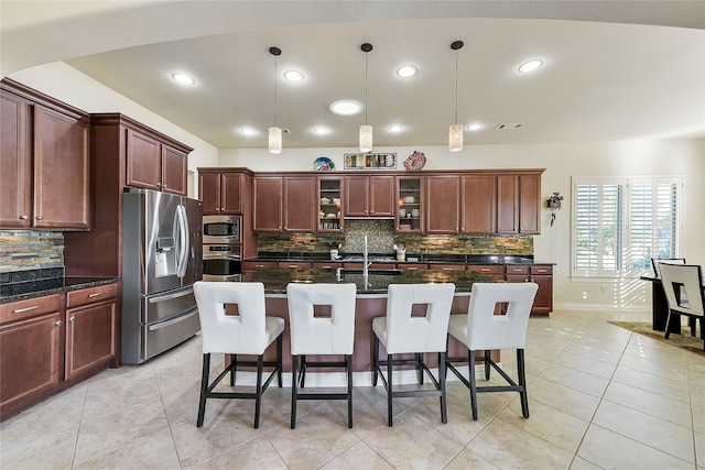 kitchen with pendant lighting, decorative backsplash, dark stone countertops, an island with sink, and stainless steel appliances