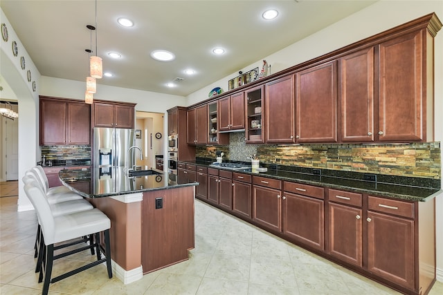 kitchen featuring sink, stainless steel appliances, backsplash, an island with sink, and a breakfast bar