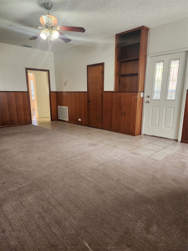 unfurnished living room featuring a textured ceiling, wood walls, ceiling fan, and light colored carpet