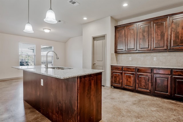 kitchen with dark brown cabinetry, decorative light fixtures, sink, light stone countertops, and an island with sink