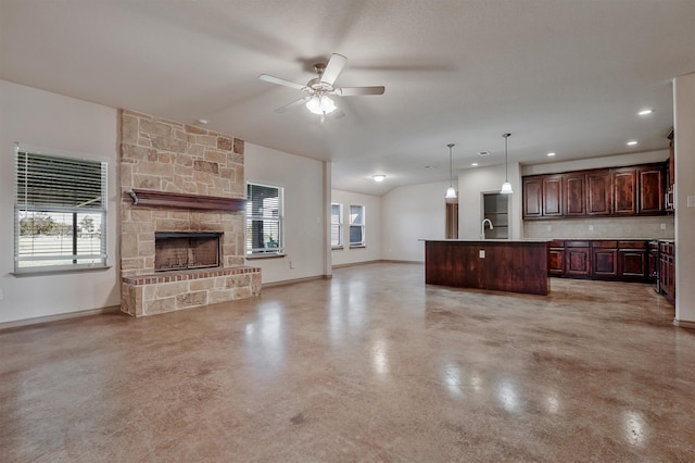 kitchen featuring an island with sink, ceiling fan, a stone fireplace, sink, and hanging light fixtures