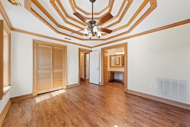 unfurnished bedroom with ornamental molding, wood-type flooring, a tray ceiling, and connected bathroom