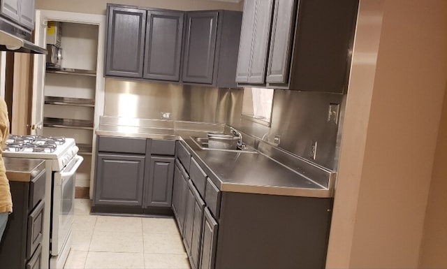 kitchen with white gas range, light tile patterned flooring, sink, and stainless steel counters