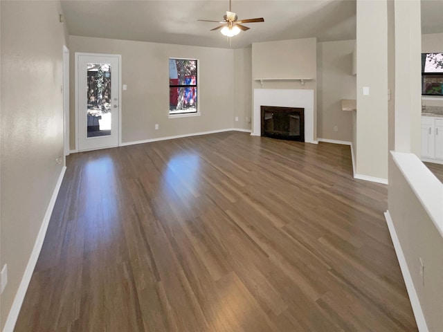 409 Misty Oaks St, Azle, TX 76020 - unfurnished living room featuring dark wood-style flooring, ceiling fan, baseboards, and a glass covered fireplace