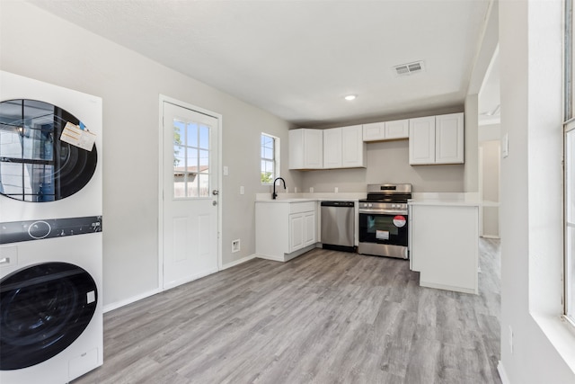 kitchen with sink, white cabinetry, stacked washer and dryer, appliances with stainless steel finishes, and light wood-type flooring