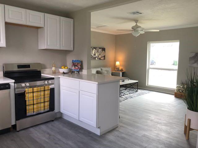 kitchen with dark wood-type flooring, white cabinetry, crown molding, appliances with stainless steel finishes, and kitchen peninsula