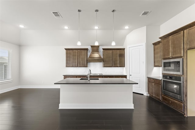 kitchen featuring pendant lighting, stainless steel appliances, dark hardwood / wood-style floors, an island with sink, and custom exhaust hood