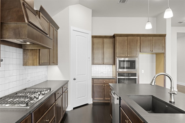 kitchen with decorative backsplash, custom range hood, sink, stainless steel appliances, and hanging light fixtures