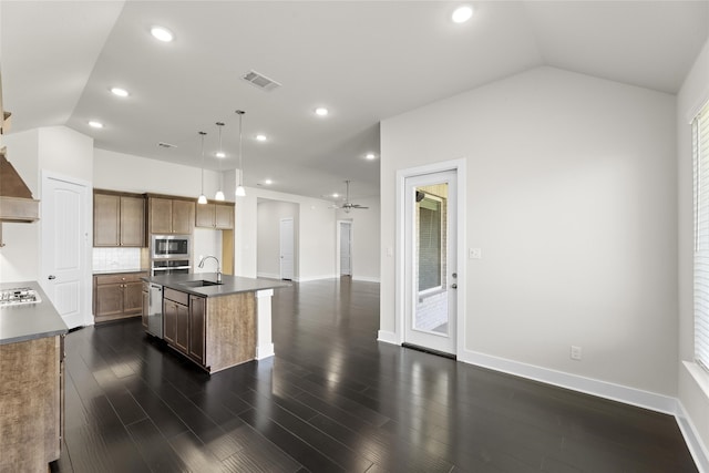 kitchen with dark wood-type flooring, decorative light fixtures, sink, lofted ceiling, and an island with sink