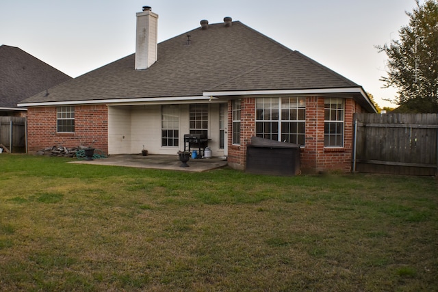 back house at dusk with a patio and a lawn