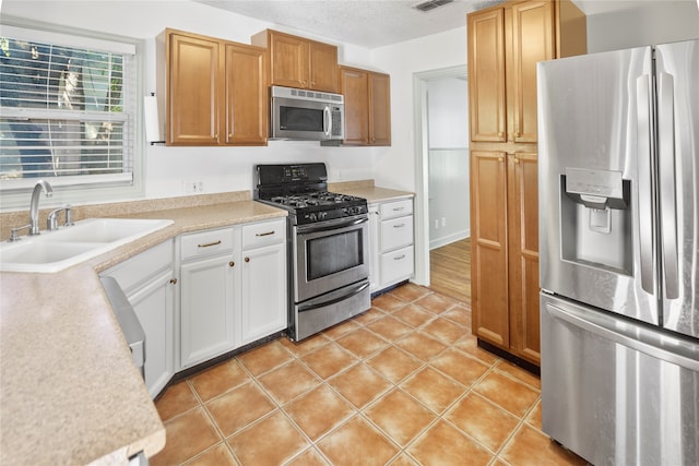 kitchen featuring white cabinetry, light tile patterned floors, stainless steel appliances, a textured ceiling, and sink