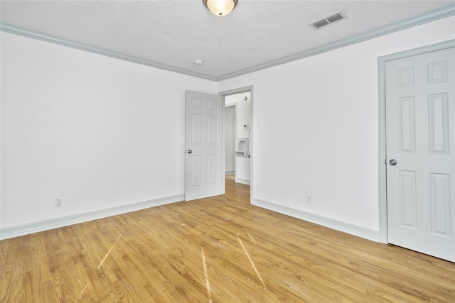 empty room with a textured ceiling, wood-type flooring, and ornamental molding