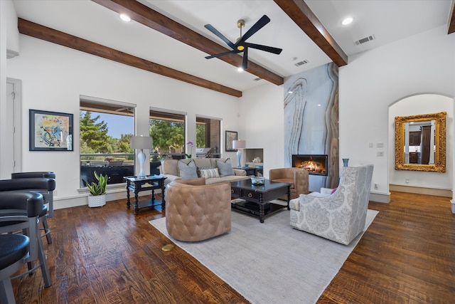 living room featuring a large fireplace, beam ceiling, ceiling fan, and dark hardwood / wood-style flooring