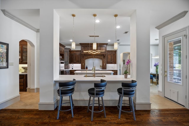 kitchen with hanging light fixtures, a breakfast bar, kitchen peninsula, dark brown cabinetry, and hardwood / wood-style floors