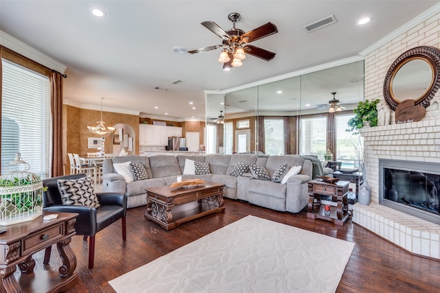 living room featuring ceiling fan with notable chandelier, ornamental molding, a fireplace, and dark hardwood / wood-style flooring