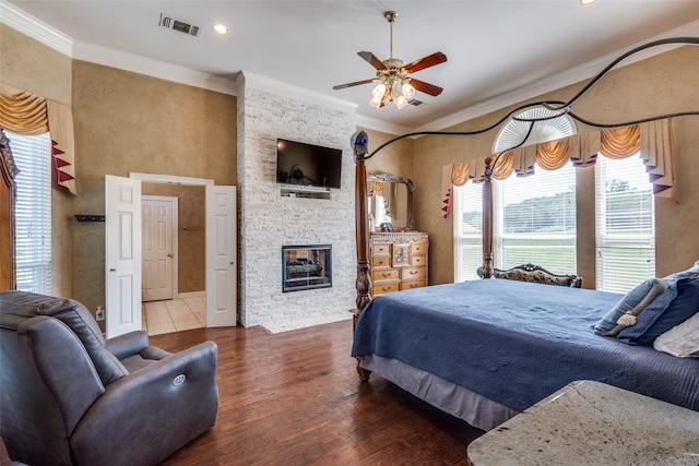 bedroom featuring a stone fireplace, ornamental molding, ceiling fan, and hardwood / wood-style flooring