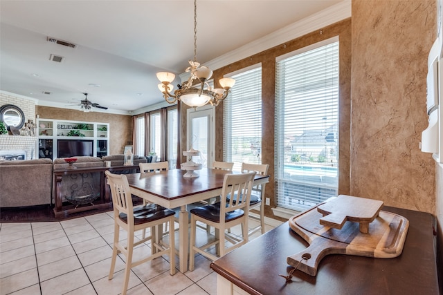 tiled dining room featuring ceiling fan with notable chandelier, a fireplace, a healthy amount of sunlight, and crown molding