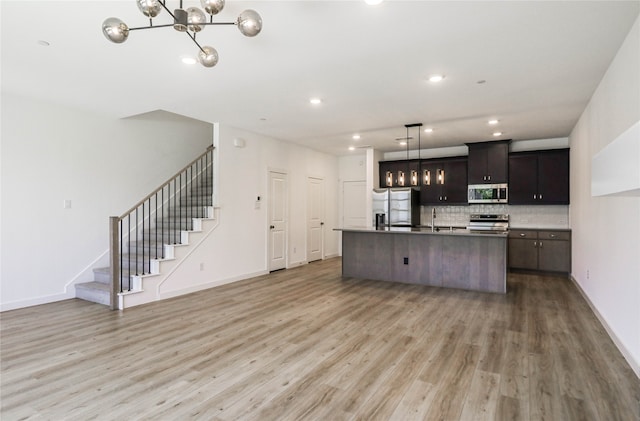 kitchen featuring light hardwood / wood-style flooring, backsplash, a center island with sink, appliances with stainless steel finishes, and dark brown cabinetry