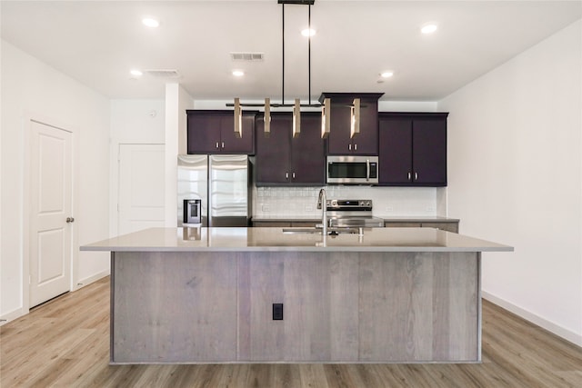 kitchen with stainless steel appliances, light wood-type flooring, decorative light fixtures, a kitchen island with sink, and sink