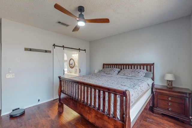 bedroom with dark wood-type flooring, ceiling fan, connected bathroom, a textured ceiling, and a barn door