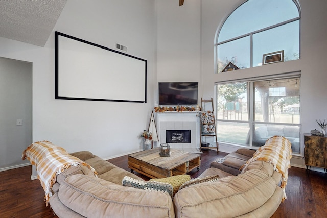 living room with a tile fireplace, dark hardwood / wood-style floors, and a high ceiling