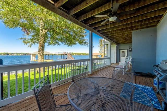 wooden deck with a water view, ceiling fan, and a lawn