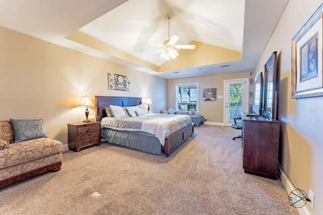 carpeted bedroom with access to exterior, a tray ceiling, and ceiling fan