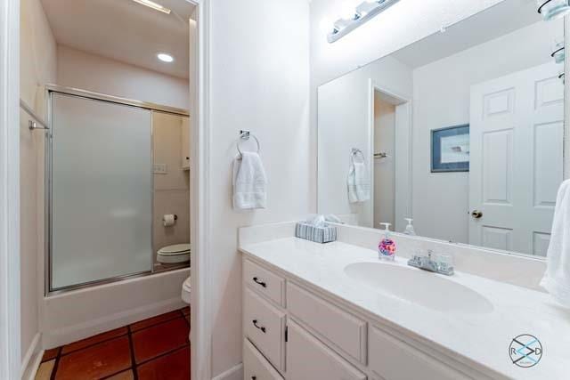 full bathroom featuring vanity, tile patterned flooring, combined bath / shower with glass door, and toilet