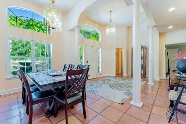 tiled dining space featuring ornate columns, a towering ceiling, and an inviting chandelier