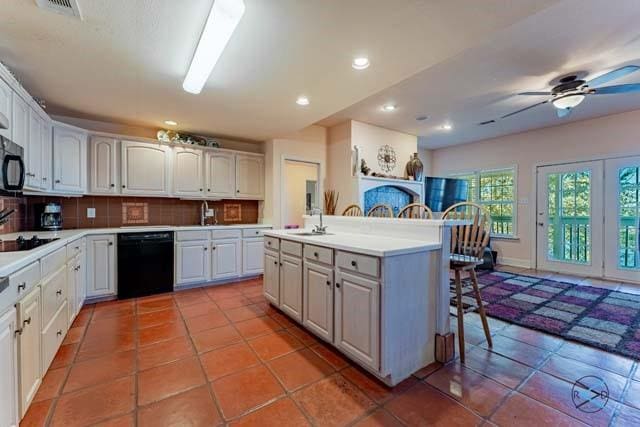 kitchen with a breakfast bar, black appliances, a center island, decorative backsplash, and white cabinets