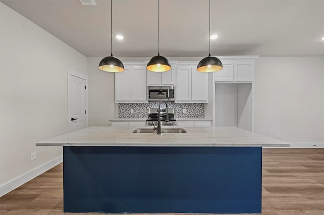 kitchen featuring light stone counters, white cabinets, pendant lighting, sink, and a kitchen island with sink