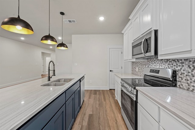 kitchen with appliances with stainless steel finishes, white cabinets, light hardwood / wood-style flooring, decorative light fixtures, and sink