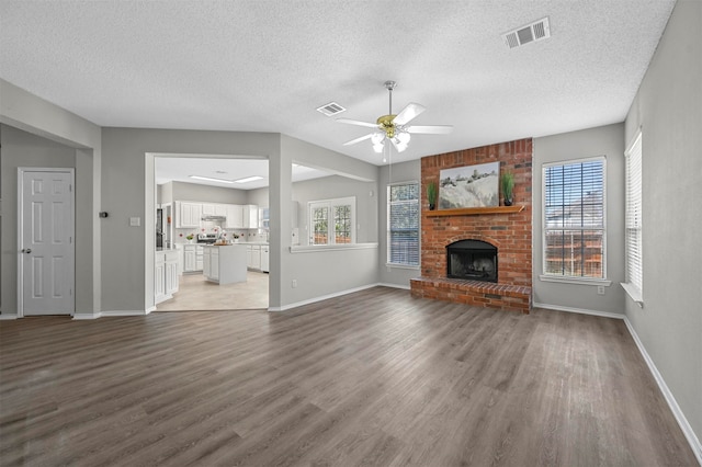 unfurnished living room featuring a textured ceiling, ceiling fan, a brick fireplace, and hardwood / wood-style flooring