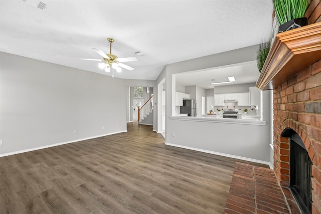 unfurnished living room featuring a textured ceiling, sink, a fireplace, dark hardwood / wood-style flooring, and ceiling fan