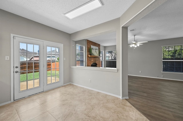 spare room with ceiling fan, a textured ceiling, light hardwood / wood-style flooring, and a fireplace