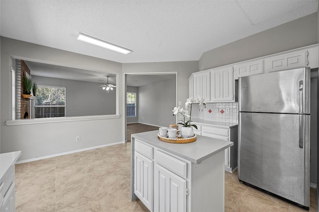 kitchen with ceiling fan, stainless steel fridge, tasteful backsplash, white cabinetry, and a center island