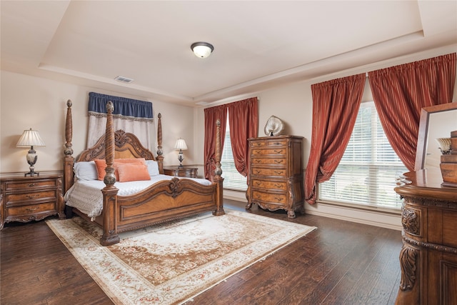 bedroom with a tray ceiling and dark wood-type flooring