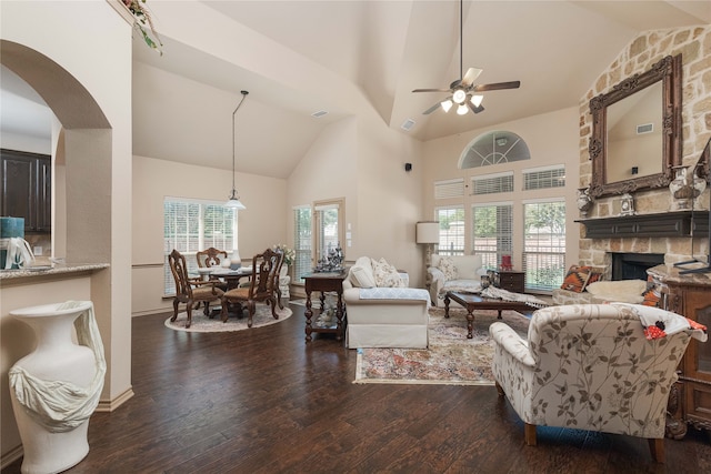 living room with high vaulted ceiling, ceiling fan, dark wood-type flooring, and a stone fireplace