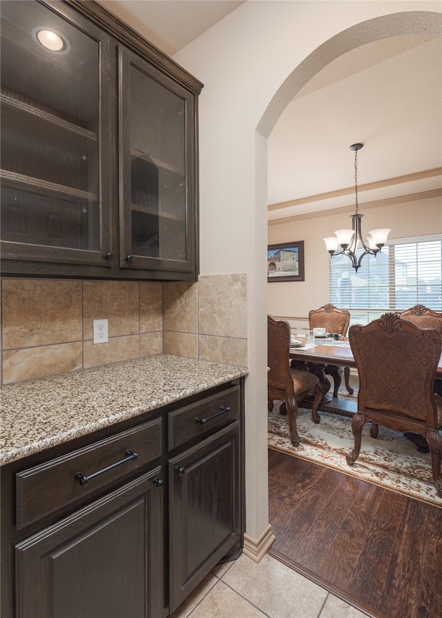 kitchen with light wood-type flooring, light stone countertops, dark brown cabinetry, tasteful backsplash, and a chandelier