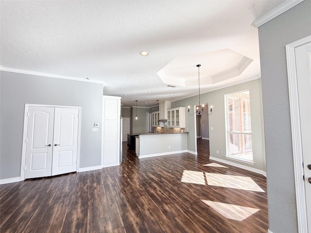 unfurnished living room with an inviting chandelier, a tray ceiling, dark wood-type flooring, a textured ceiling, and ornamental molding